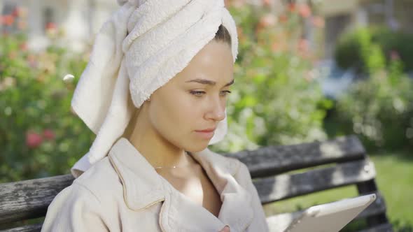 Portrait of Young Woman in Bathrobe with Towel on Head Got Shocking News While Sitting on the Bench