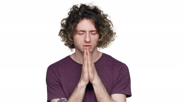 Portrait of Hopeful Young Man Wishing Something Good with Closed Eyes and Holding Palms Together for
