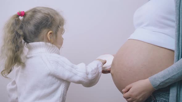 Girl in Sweater Applies Cream on Pregnant Mom Belly in Room