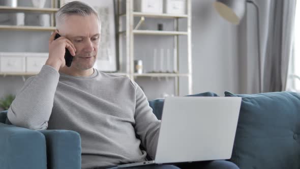 Gray Hair Man Talking on Phone While Working on Laptop