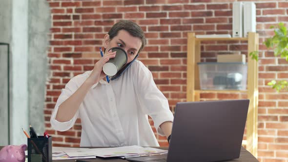 Businesswoman Communicates on Phone Drinks Coffee From a Paper Cup Working on a Laptop and Looking