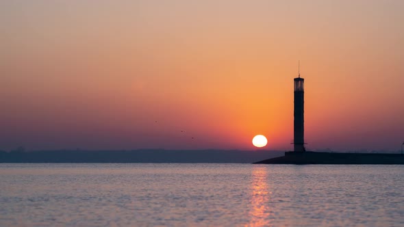 Time Lapse of a Red Sunrise Over a Vast Lake or Sea with a Lighthouse