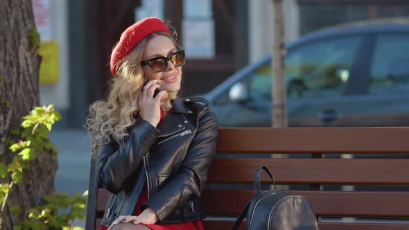 Young Beautiful Woman in a Red Beret and Dress Black Glasses and a Braid Sitting on a Park Bench