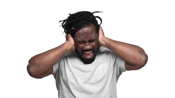 Portrait of Frightened Dark Skinned Guy with Afro Pigtails Covering Ears While Screaming Due to