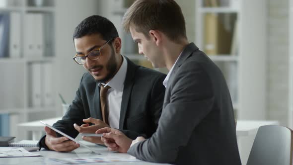 Two Businessmen Discussing Text on Tablet Screen in Office