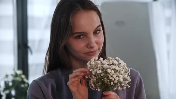 A Young Woman Holds Little White Flowers and Looks in the Camera