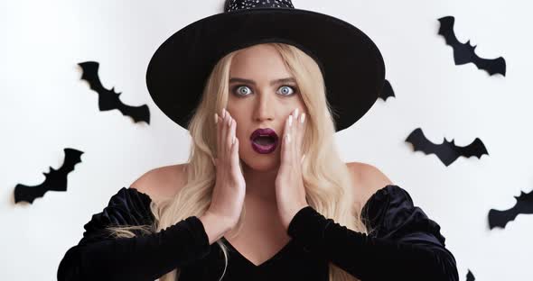 Shocked Young Blonde Woman in Witch Costume Surprising Around, Touching Her Face