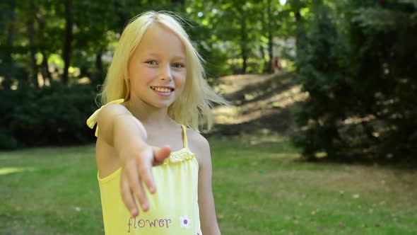 Little Cute Happy Girl Stands in the Park and Shakes with Hand for Welcome