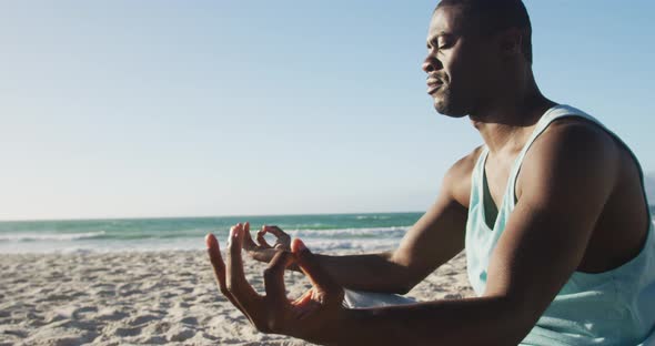 Focused african american man practicing yoga on beach, exercising outdoors by the sea