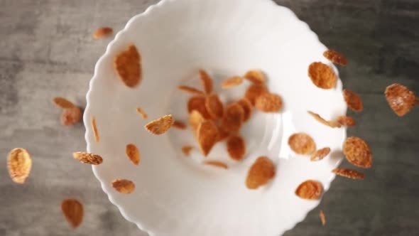 Corn Flakes are Pouring Into White Bowl Standing on Wooden Surface in Slowmo