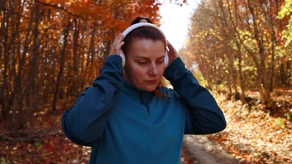 Active Sport Woman in Sportswear with White Wireless Headphones Running Along Outdoor in Fall Forest
