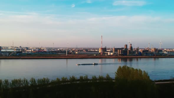 Cargo ship cruising on river by industrial area, drone lowering shot