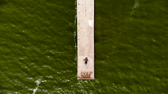 AERIAL: Flying Over Green Sea Towards Shore Above Stone Bridge