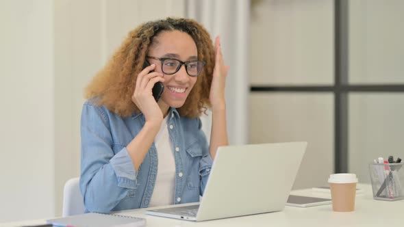 Angry African Woman Talking on Smartphone While Using Laptop