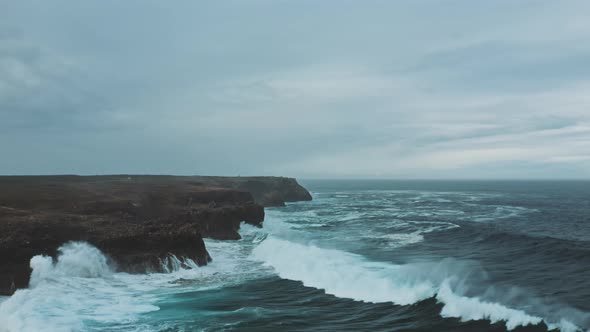 Wild ocean waves crashing againt coastal cliffs and into the caves shot by drone