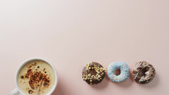 Video of donuts with icing and cup of coffee on pink background