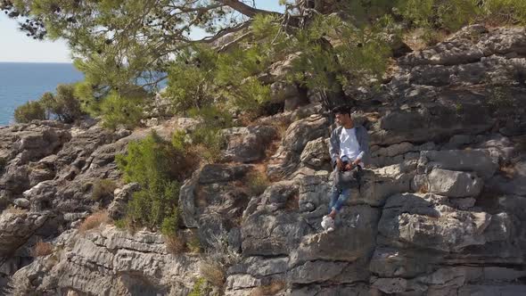 Aerial View of Young Man Traveler on Rock Cliff Against Sea