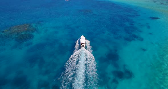 Aerial drone view of a motor boat going to a scenic tropical island in the Maldives.