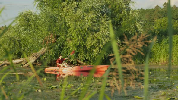 Sportive woman sails in boat on calm river. Female tourist is rowing in canoe on lake in summer.