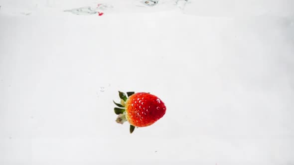 Strawberries with Leaves Immersed in Water at a Slow Motion on an Isolated White Background