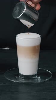 Barista pouring milk in hot coffee and making cappuccino foam in cafe close up, vertical