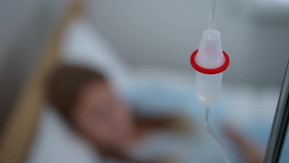Closeup Medical Dropper in Hospital Ward with Blurred Caucasian Patient Lying in Bed at Background