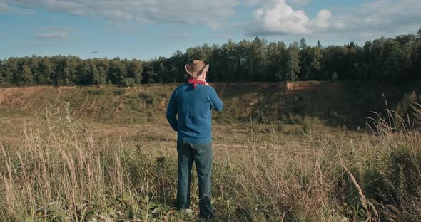 Man in Cowboy Hat Stand on Edge of Sandy Ravine Overgrown with Forest