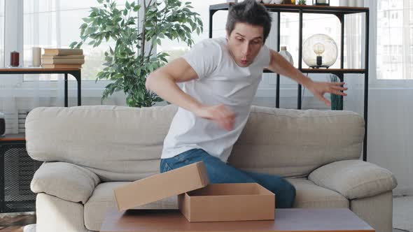 Caucasian Millennial Adult Man Buyer Consumer Receives Parcel Sitting on Couch Opening Cardboard Box