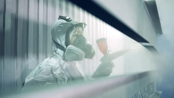 A Woman in Safety Wear is Spraying Paint on Metal