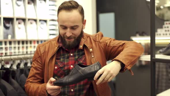 Stylish Young Man Stands With Shoes In Hands In Store And Smiling.