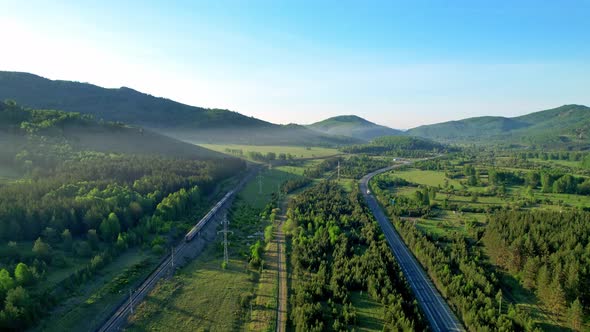 Railway tracks and a highway in the middle of the forest and mountains.