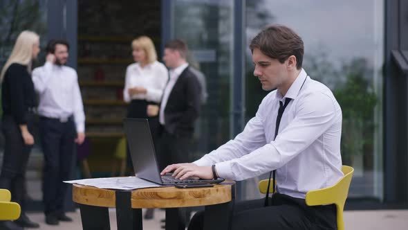 Side View Concentrated Man Typing on Laptop Keyboard Sitting on Office Terrace with Blurred