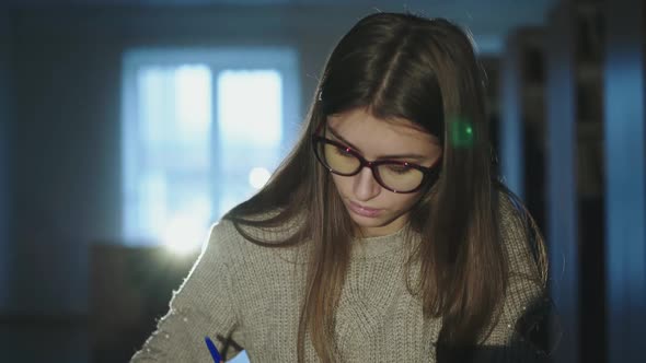 Girl in Glasses Thinks While Taking Notes Articles From Books in the Library