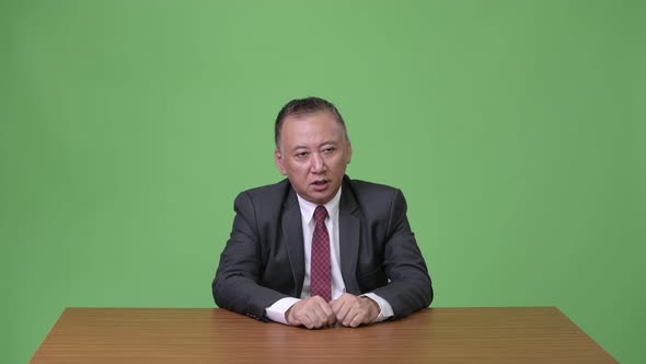 Mature Japanese Businessman Talking Against Green Background