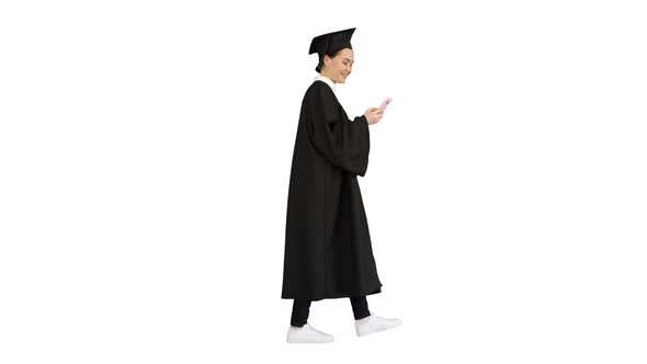 Smiling Female Graduate in Mortarboard Texting on Her Phone While Walking on White Background