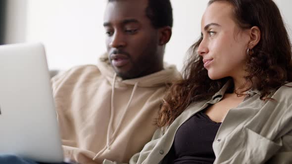 Relaxed Young Couple At Home Sitting On Sofa Browsing Internet On Laptop Computer