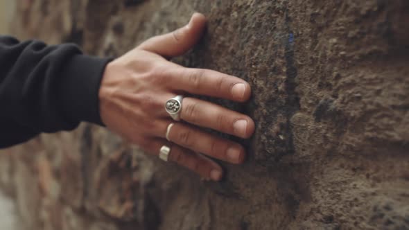 Caucasian hands with silver rings drag along, feeling the stone wall