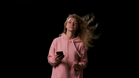 Beautiful Lovely Woman in Pink Sweatshirt with Hood Gets Call on Phone on Black Background. Lady