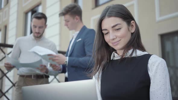 Portrait of Pretty Young Woman in the Foreground Working with Laptop. Two Successful Confident Men