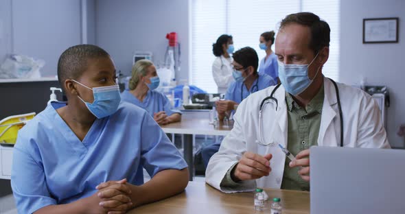 Diverse male and female doctor talking, man preparing covid vaccination, both wearing face masks