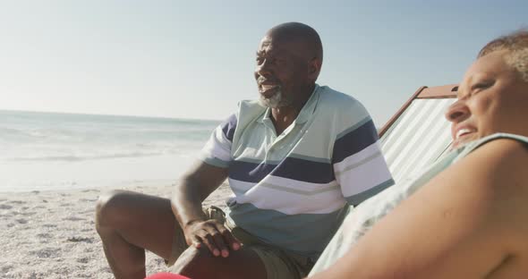 Smiling senior african american couple lying on sunbeds on sunny beach