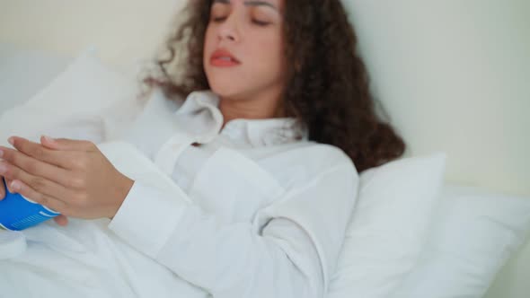 Young Latino sick woman in pajamas take medicine after wake up on bed. Health care-medical lifestyle