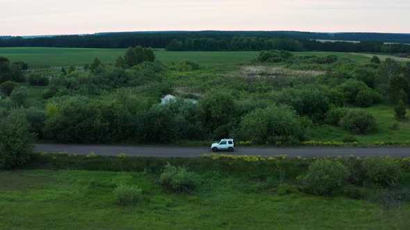 Aerial View of a Car Driving in Nature on a Field at Sunset