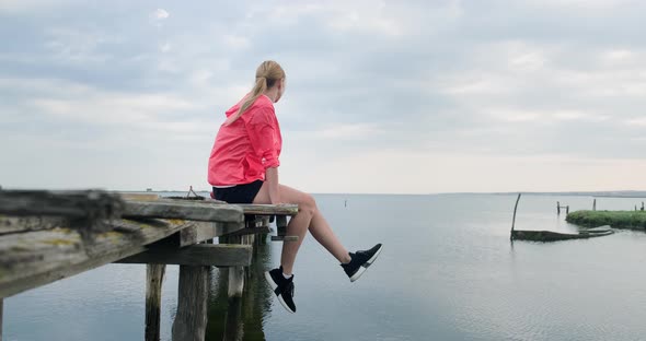 Woman sitting with her legs dangling on old wooden pier.