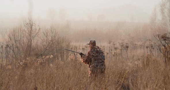 Hunter in Hunting Equipment With a Rifle in His Hands Sneaks Through the Dry Grass to the Target