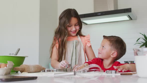 Happy caucasian siblings baking together, preparing cookies in kitchen