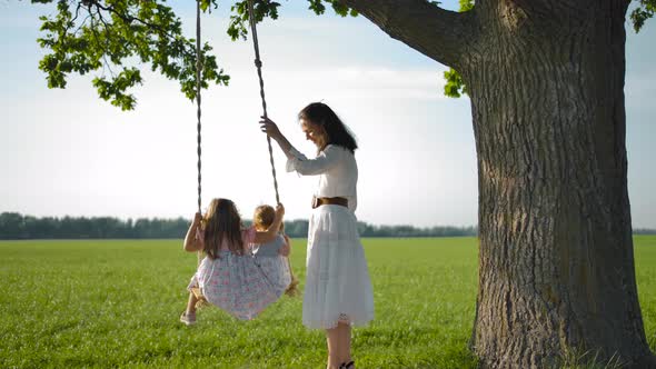 Cute Mom Swings Her Daughters on a Rope Swing Tied To an Old Tree.