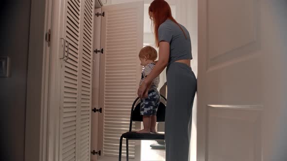 Ginger Woman Moves the Chair with Her Baby Standing on It and Closes the Wardrobe