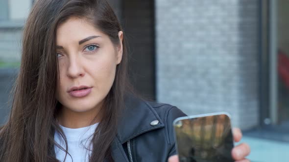 Upset Woman Looks at a Smartphone and Shows His Broken Screen.