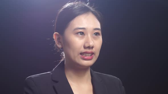 Side View Of Asian Speaker Woman In Business Suit Speaking In The Black Screen Studio